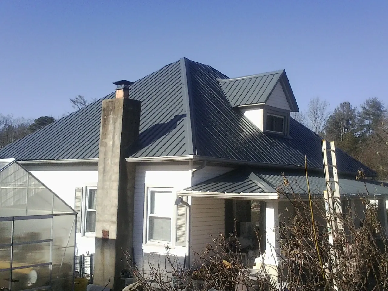 Dark blue standing seam metal roof on a white farmhouse with dormer — Slate & Tile Roof Repair by Roofing Brothers in Clayville