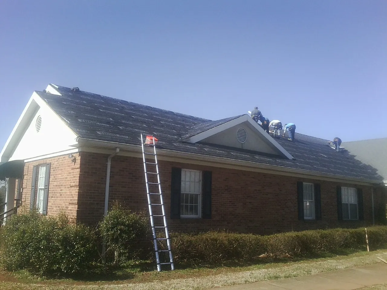 Crew tearing shingles off a brick ranch roof with a ladder set — Emergency Roof Repair work by our crew in Clayville