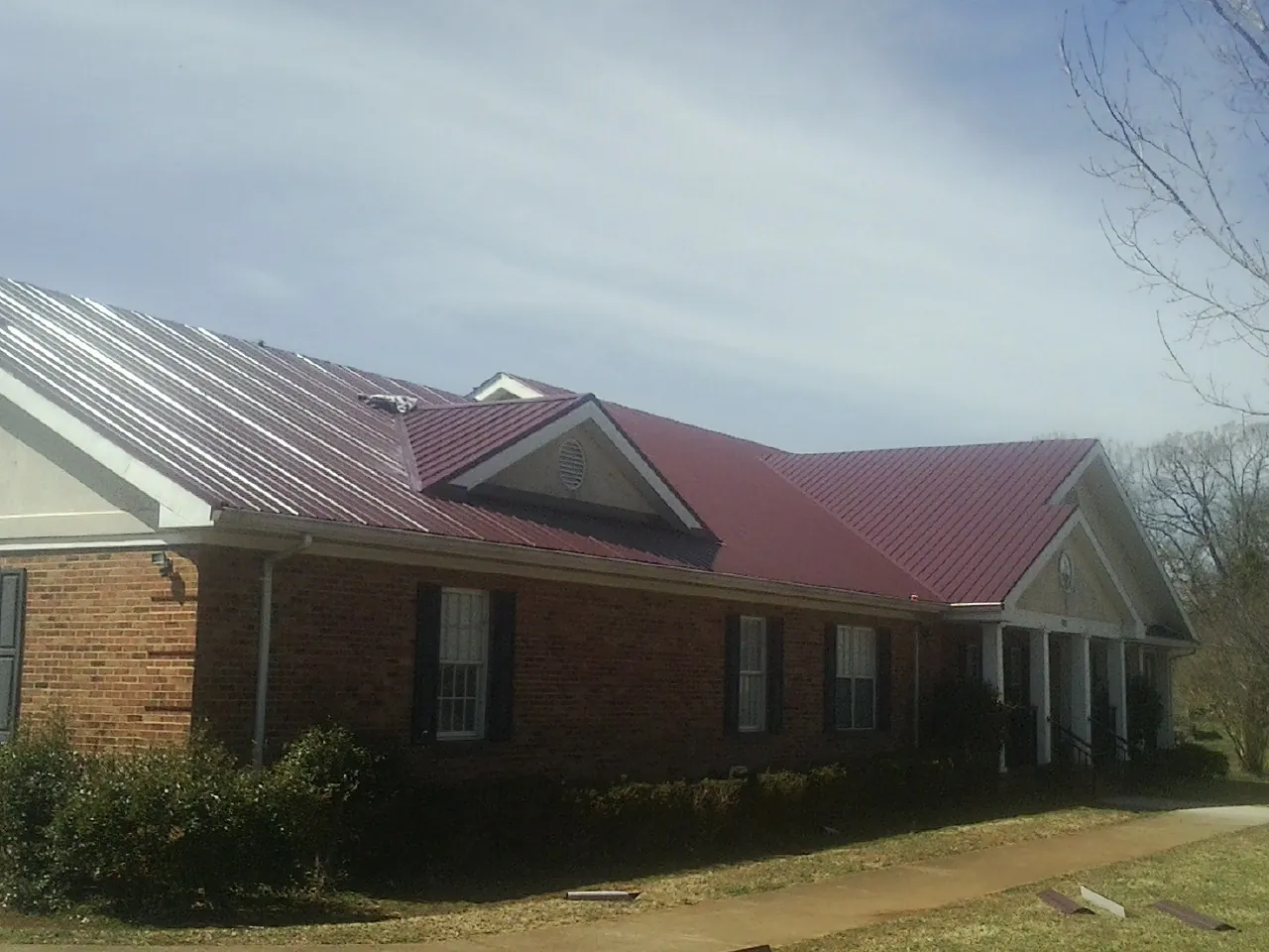 Red metal roof with gabled entries on a long brick building, from a Hail Damage Roof Repair job in Clayville