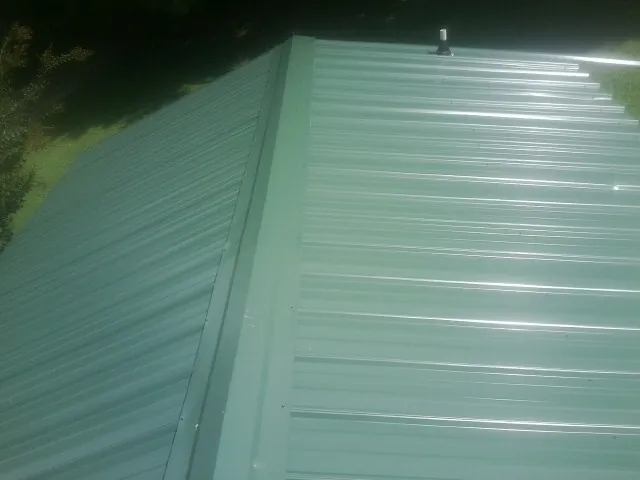 New green metal panels meeting at the ridge of a roof — Flat Roof Repair work by our crew in Clayville