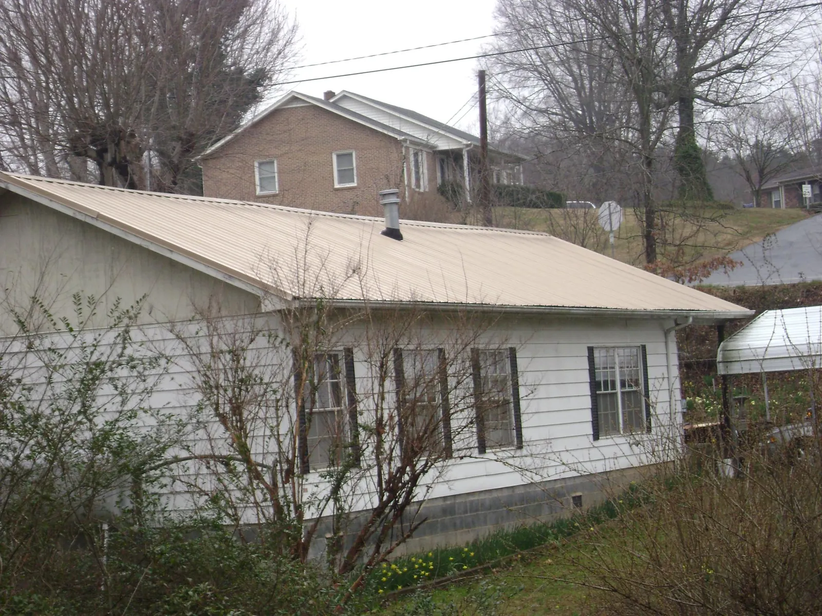 Tan metal roof on a white sided house set into a hillside — Commercial Roofing by Roofing Brothers in Clayville